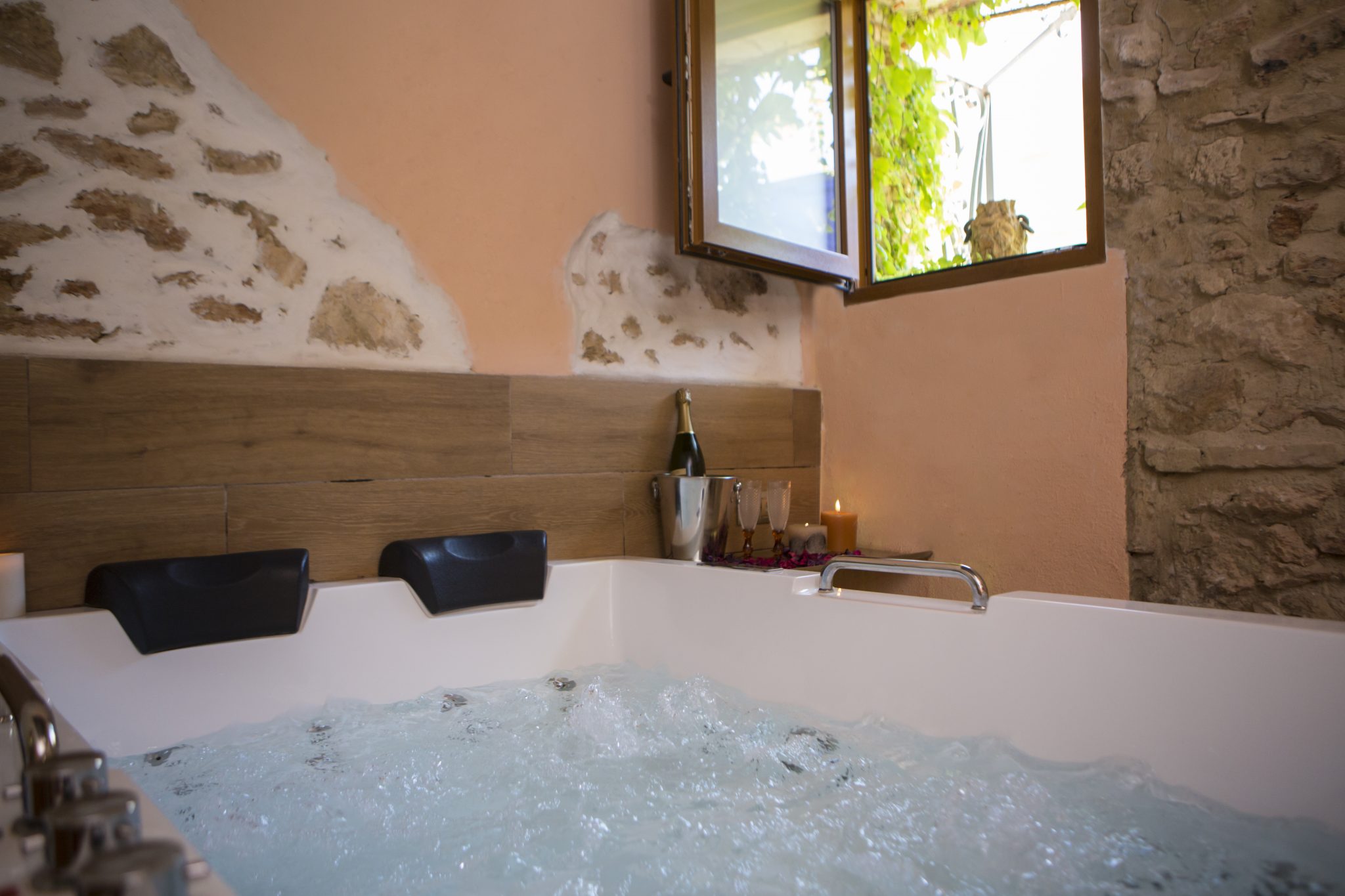 Bañera de hidromasaje/jacuzzi con dos reposacabezas con una botella de champagne o cava, velas y dos copas, también una ventana abierta